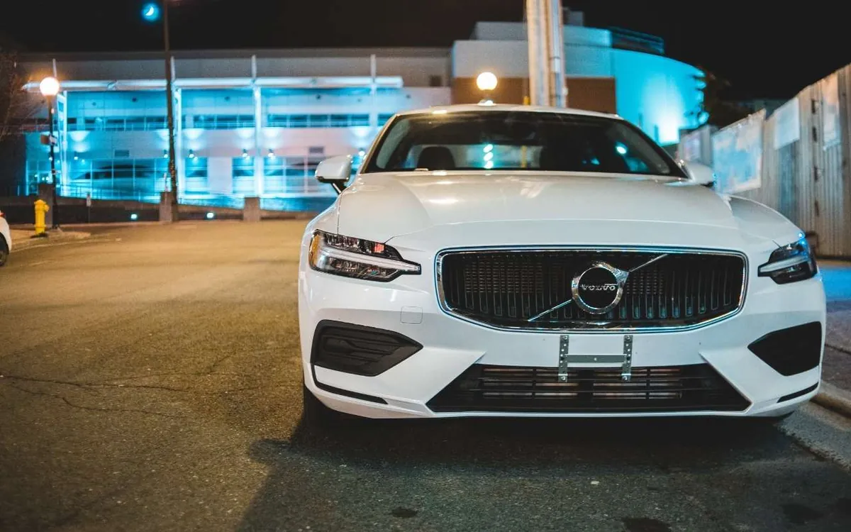 White Volvo wagon parked at night in front of a cyan-lit building
